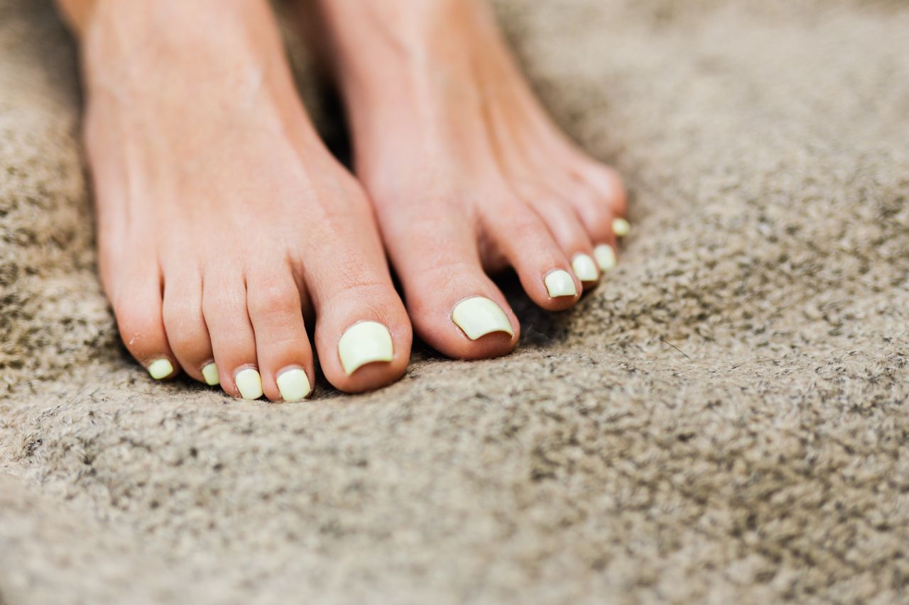 Close-up of a woman's feet with a fresh pedicure on a soft beige blanket.