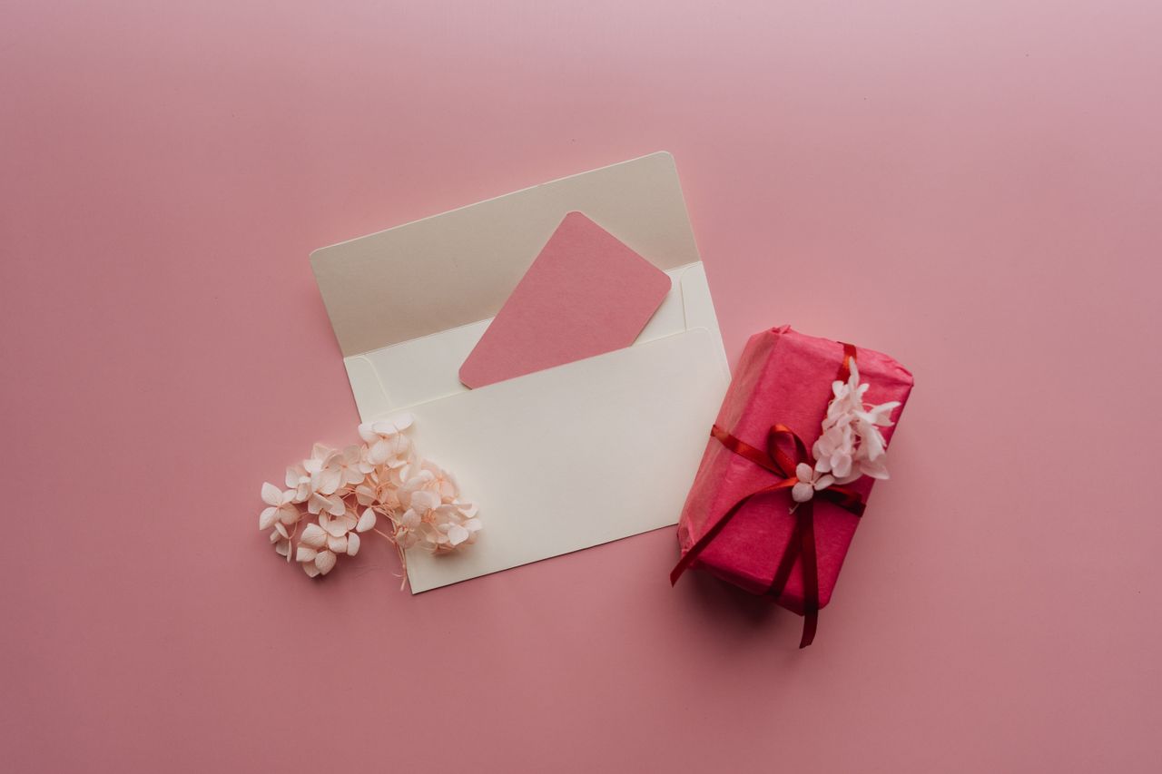 Top-down shot of a wrapped pink gift and envelope with flowers on a pink background.